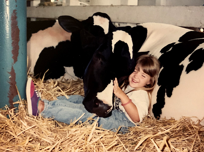 Childhood photo of Dr. Delaine Quaresma sitting next to a cow