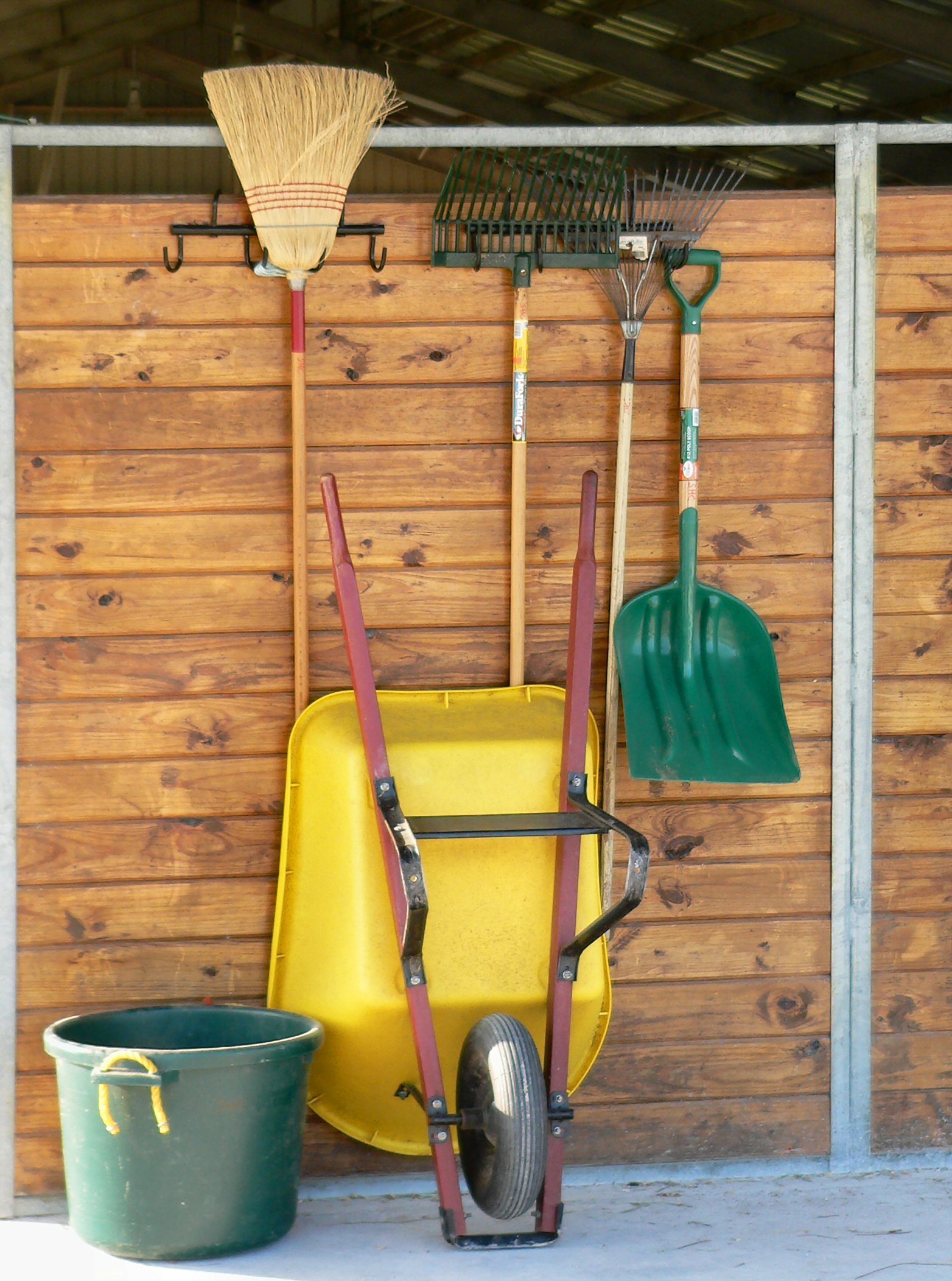 Wheelbarrow, shovel, and various tools are propped up against a wood wall.